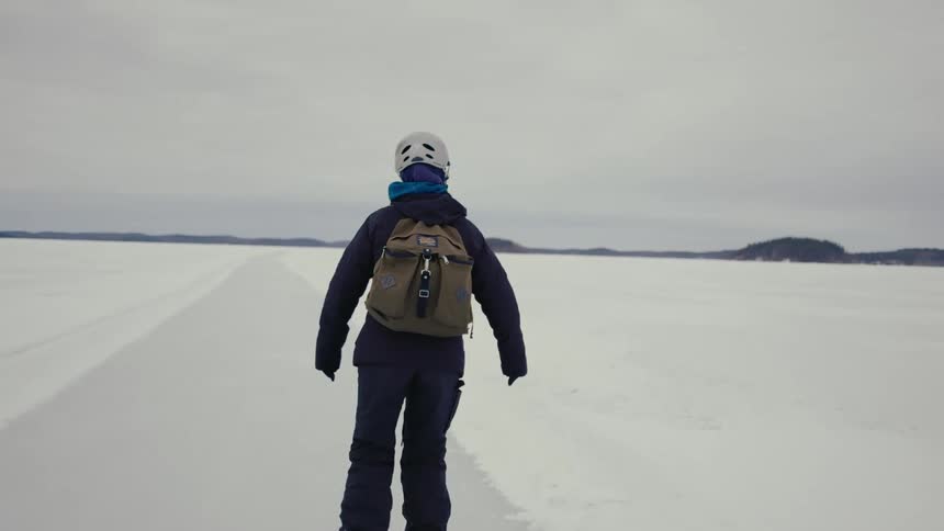 Camera follows a woman as she ice skates across a frozen lake