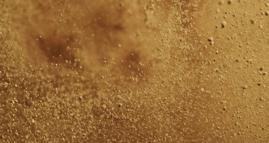 Extreme closeup on the ground with sand exploding in slow motion