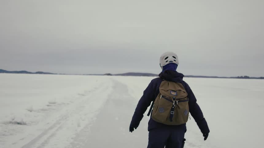 Camera follows a woman ice skating outdoors on frozen like on a cloudy day