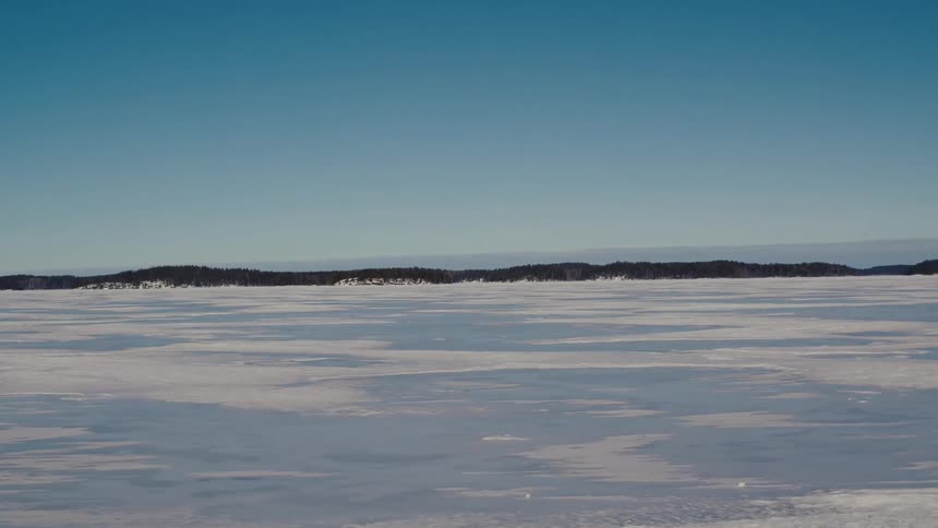 A wide view of a frozen lake with a forest in the distance