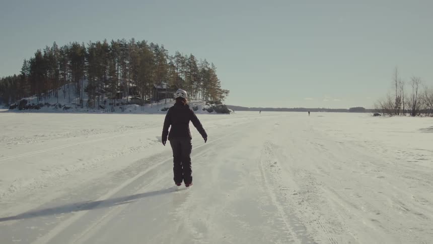 View of a woman from behind ice skating in a natural outdoor location with the sun shining