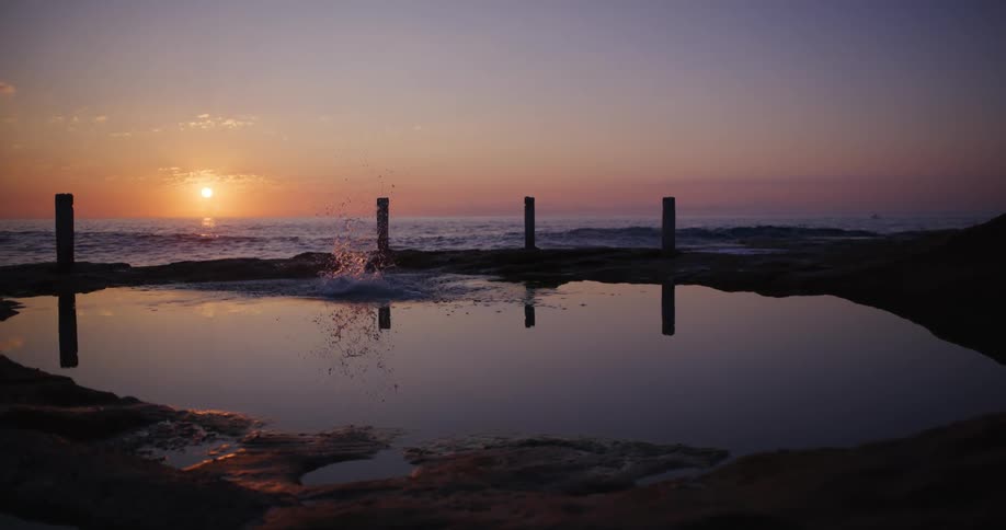 Silhouette of a man jumping into a natural pool in front of the sea with the sunset on the horizon in a purple and reddish sky