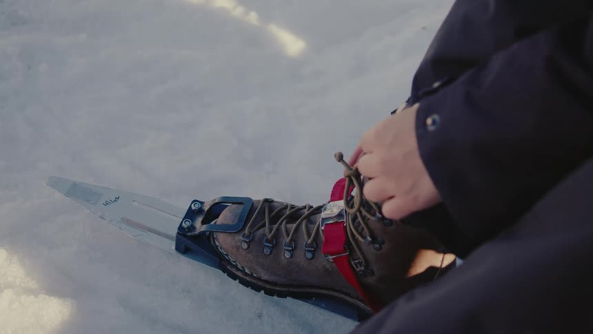 Woman with helmet attaches ice skates to her hiking boot in the snow