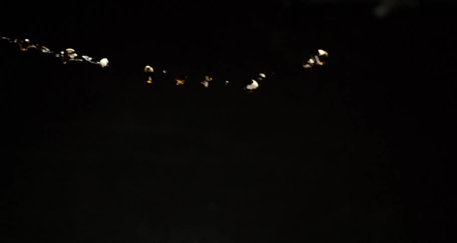 A stream of yellow liquid droplets flies over a dark background