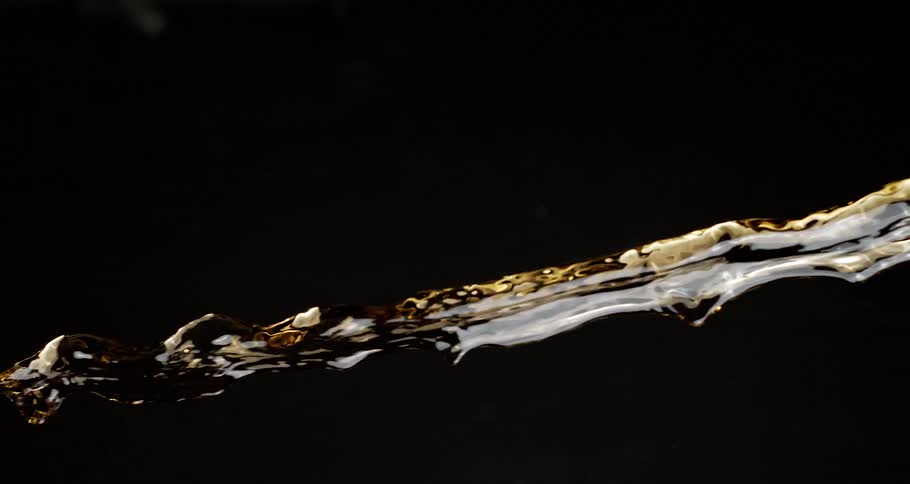 Extreme closeup on the jet of a brownish liquid on a black background and in slow motion