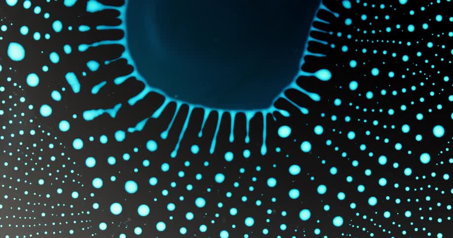 Extreme closeup of a blue liquid collapsing and forming small droplets with abstract patterns