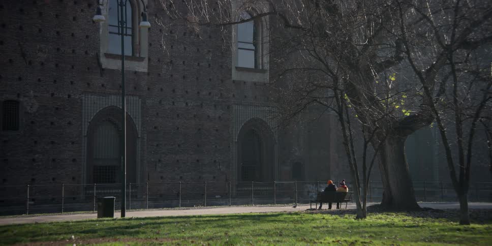 Two people sitting on a bench in a square facing the Castello Sforzesco in Milan