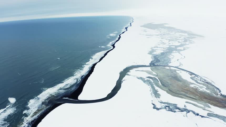 Aerial scene of a terrain covered in snow and ice with a river channel leading to the sea