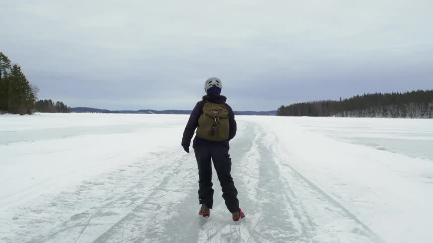 A person carrying a backpack skates on a frozen lake