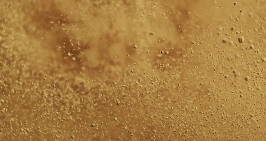 Extreme closeup of yellowish powder exploding and falling in slow motion