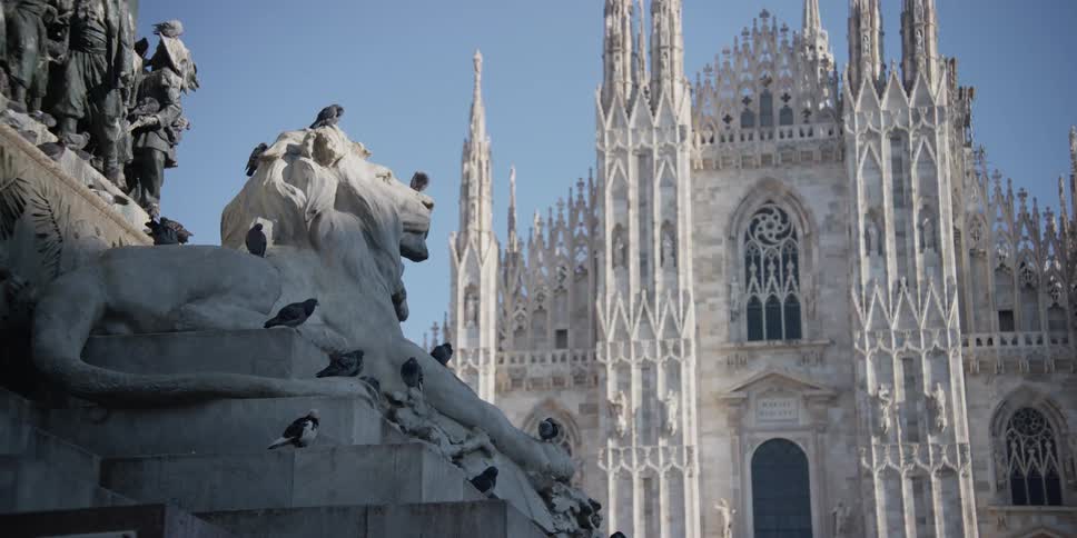 Cathedral Duomo di Milano in Milan, Italy with a statue of a lion in front of it and live pigeons all over the stone lion