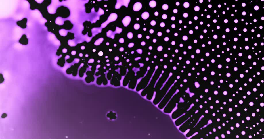 Texture of a vibrant purple liquid collapsing and forming small abstract balls on a black background