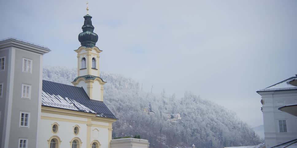 Tower of St. Michaels Church in Salzburg, Austria on the edge of mountains with snowcovered forests on a cloudy day