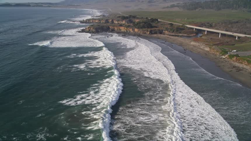 Foaming waves roll onto coast near bridge and nearby business complex