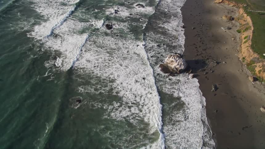 Waves crash against the shore near a large home in a rural area