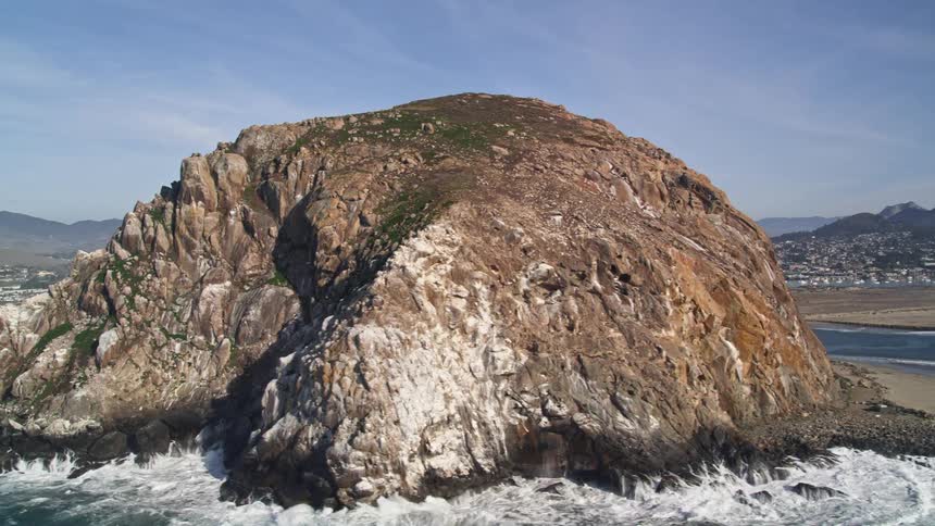 Rocky coast with calm sea and in the background a city nestled between green hills and a power plant