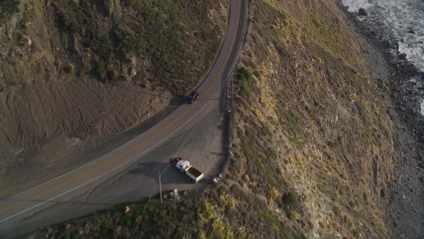 Aerial view of a vehicle traveling on a road on a seaside mountain cliff