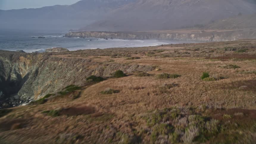 Aerial scenery of rocky coast with vegetation by the sea and mountains on the horizon