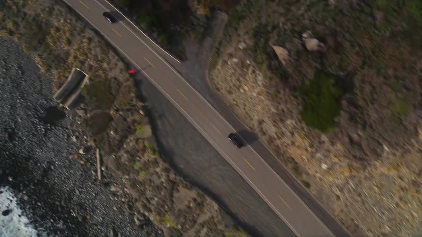 Aerial view of a paved street with vehicle traffic amid mountains and close to the sea