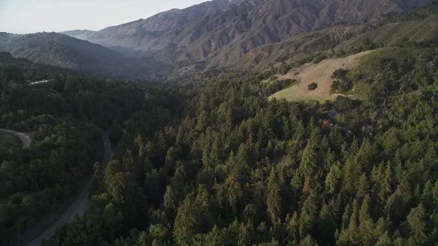 Aerial panorama of mountains with conifers and an extensive highway with a few scattered houses