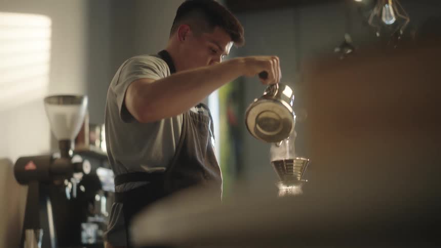 A male barista is brewing coffee using the pourover method