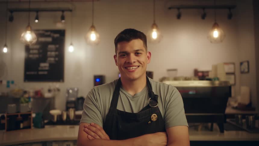 Portrait of a man with arms crossed smiling and wearing an apron while in a coffee shop