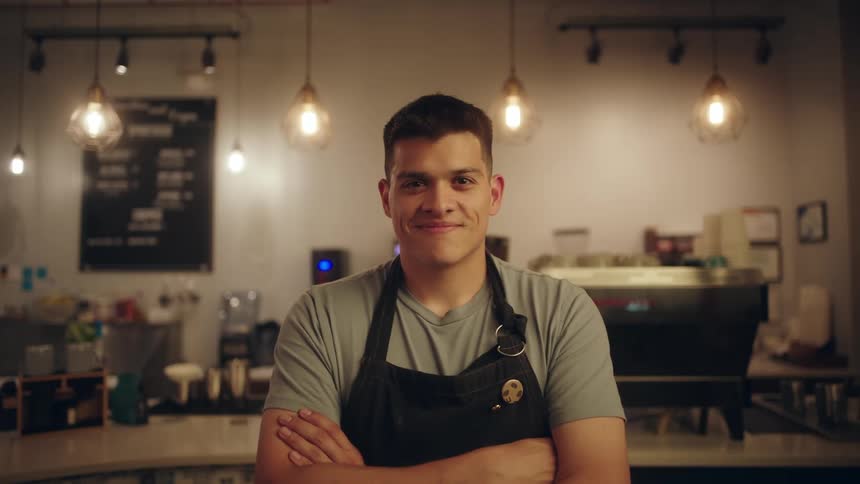Portrait of a man wearing an apron and arms crossed smiling while in a coffee shop