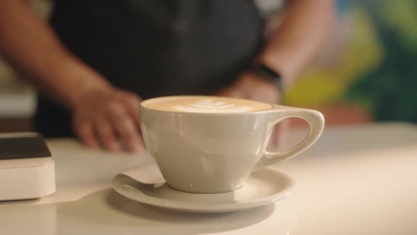 Hands of a man presenting a mug of cappuccino on a saucer