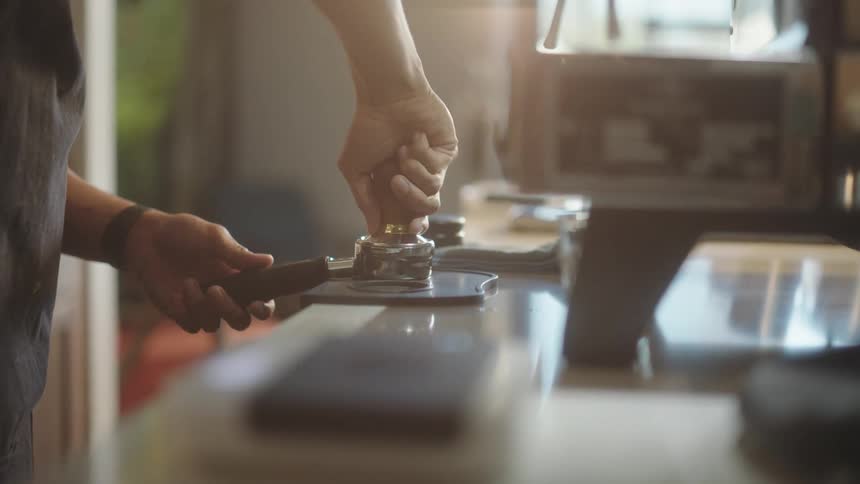 A male barista presses coffee into an espresso grinder burr before inserting it into the machine
