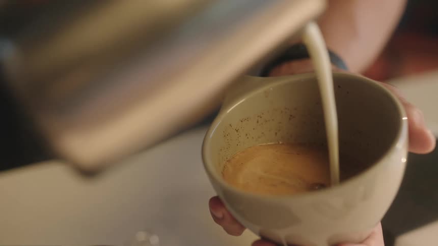 Man pours milk onto beverage in cup held in one hand