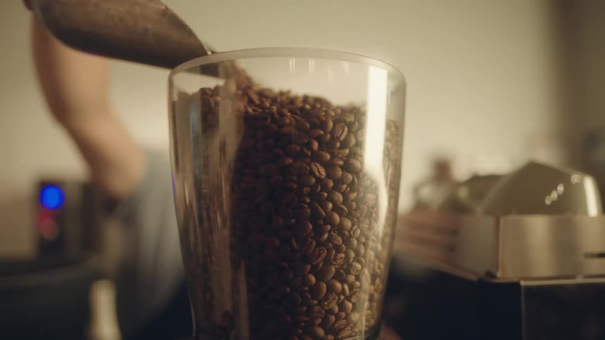 A person putting coffee beans into a glass container