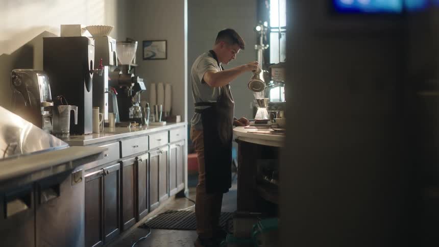A worker at a cafe pours a liquid into a coffee urn