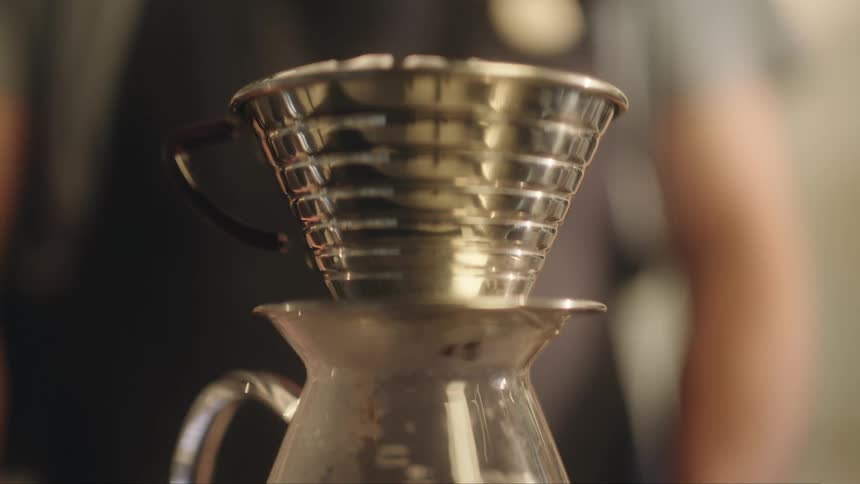 A person is making coffee using a pourover method with a metal filter