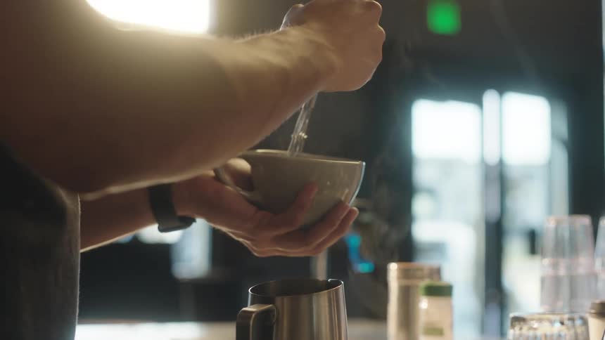 A male barista prepares a latte gently whisking the contents