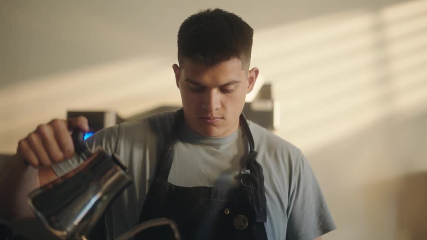 Portrait of a concentrated man holding a kettle and pouring water while in a coffee shop