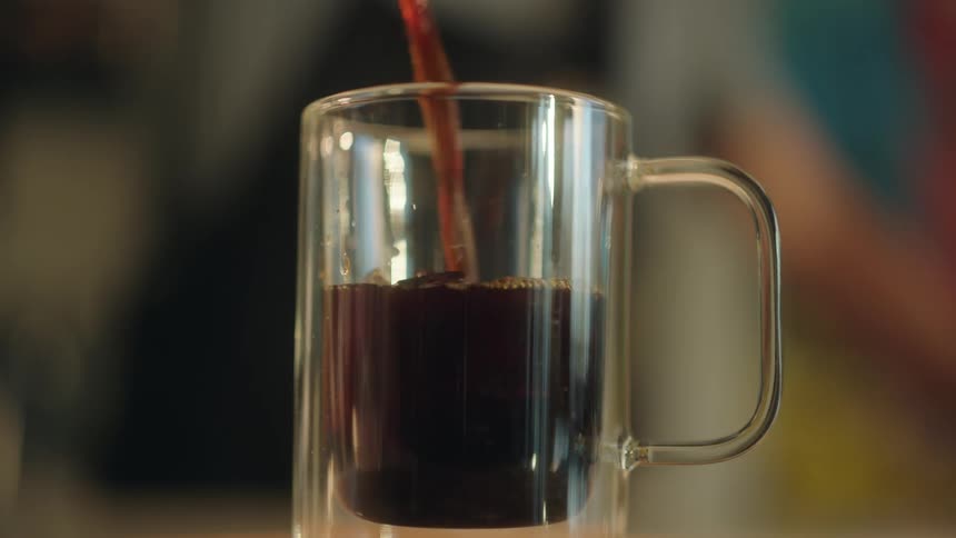A glass cup being filled with black coffee over ice