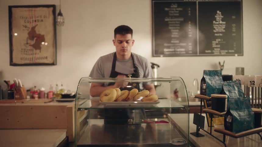 An employee at a cafe puts a tray of bagels in a display case