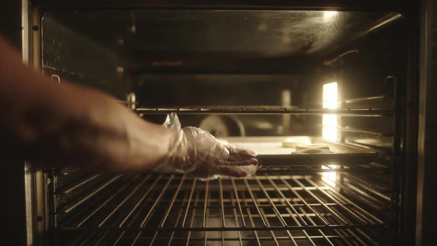 Hands of a person placing donuts to bake in an oven