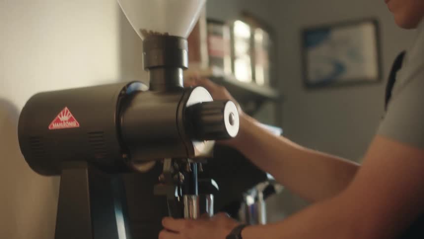 Male barista pours beans into machine at coffee shop