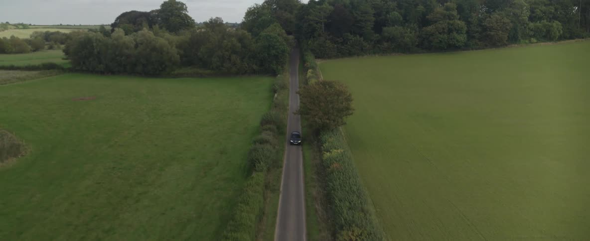 A black car travels down a country road in a grassland area