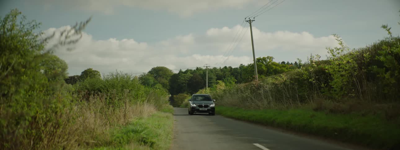 Bmw suv passing on a narrow street with trees during the day