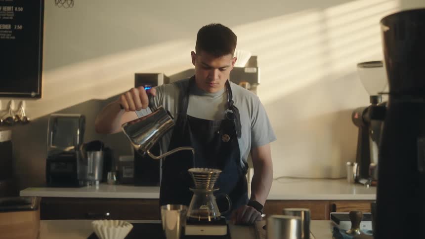 Man in an apron with a kettle pouring water into a filter and decanting a coffee