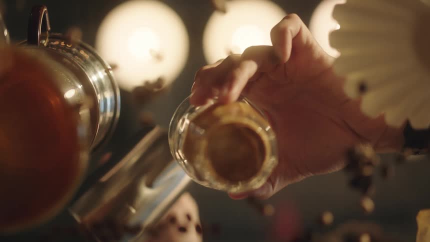 Upward view of a glass table with the reflection of a person pouring coffee into a glass cup