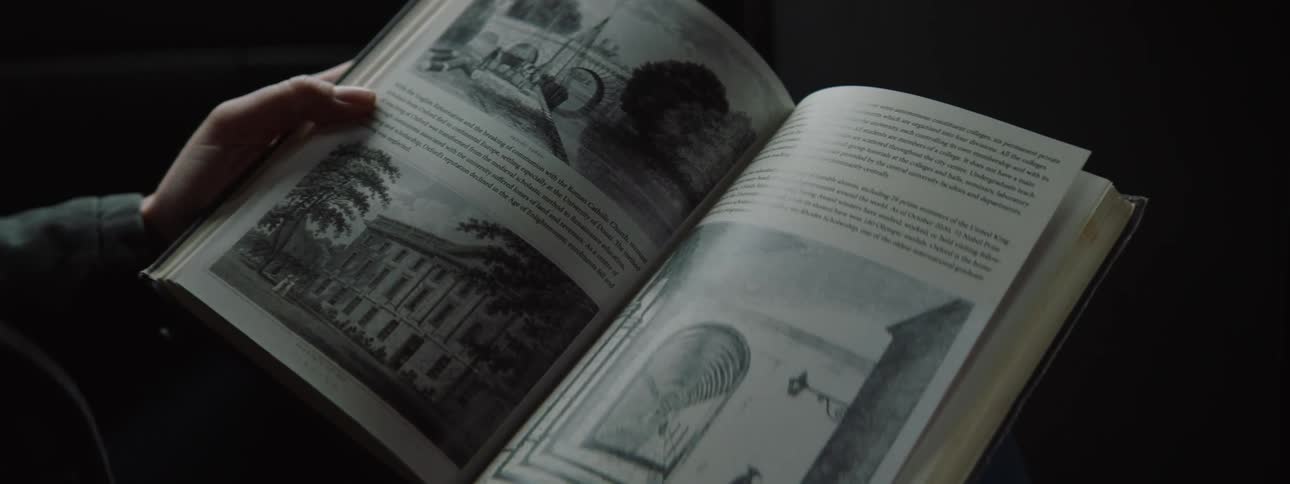 A pair of hands holding an open book with black and white illustrations