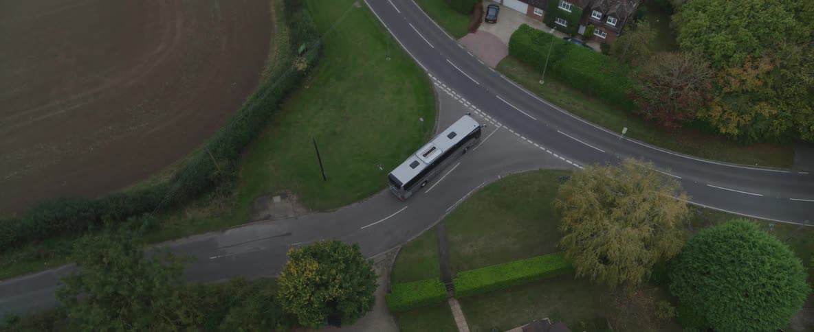 An aerial view of a white bus with a black stripe driving down a street in a residential area