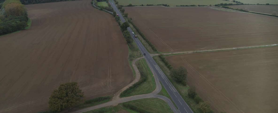 A road between two huge fields with some cars passing by
