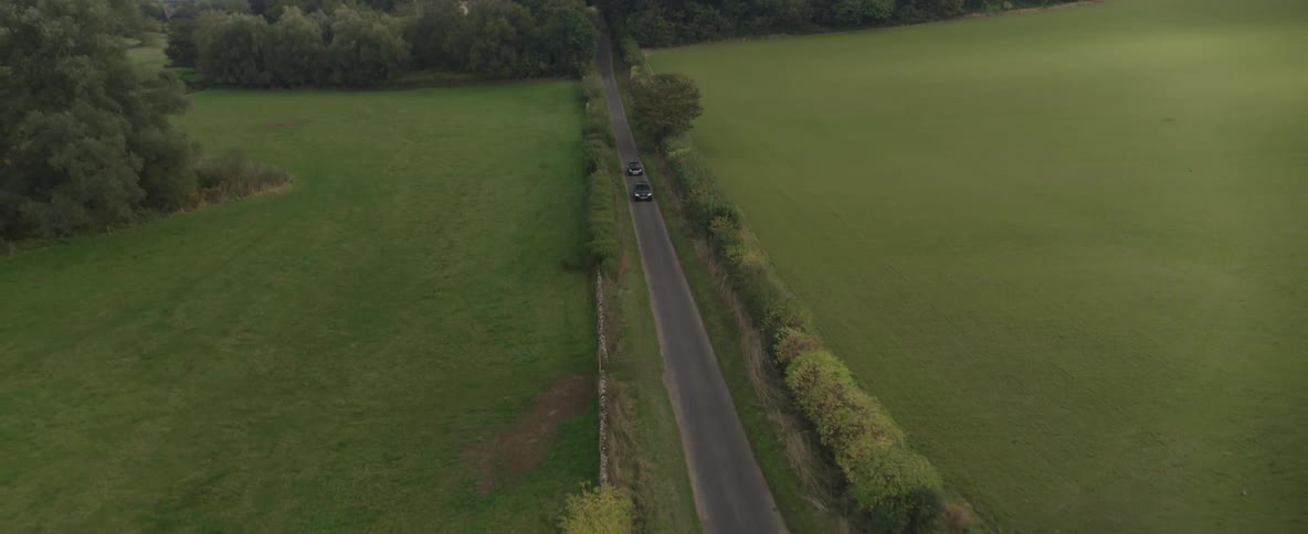 Aerial view of a couple of cars driving on a narrow country road