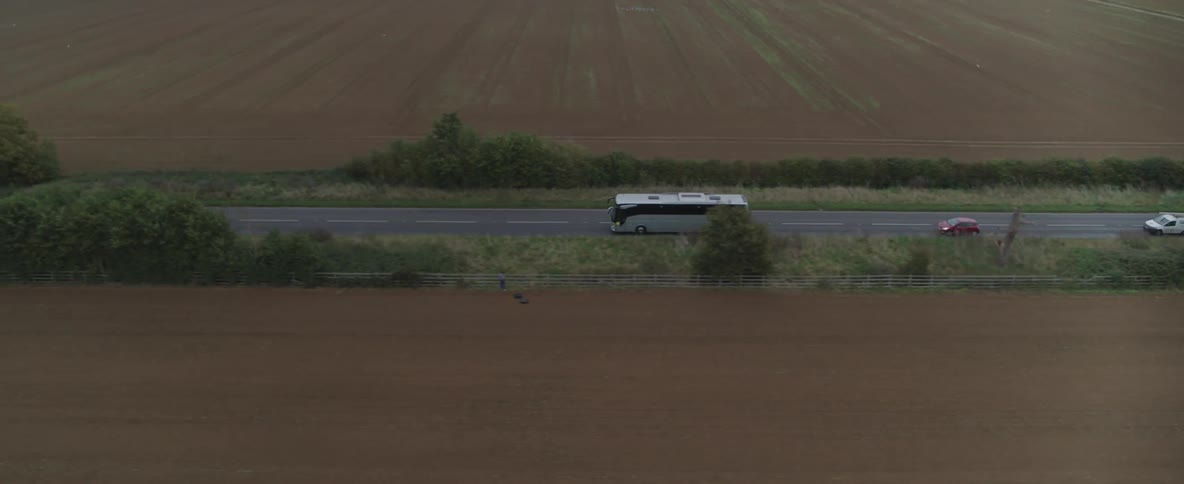 An aerial view of a bus driving on a narrow country road