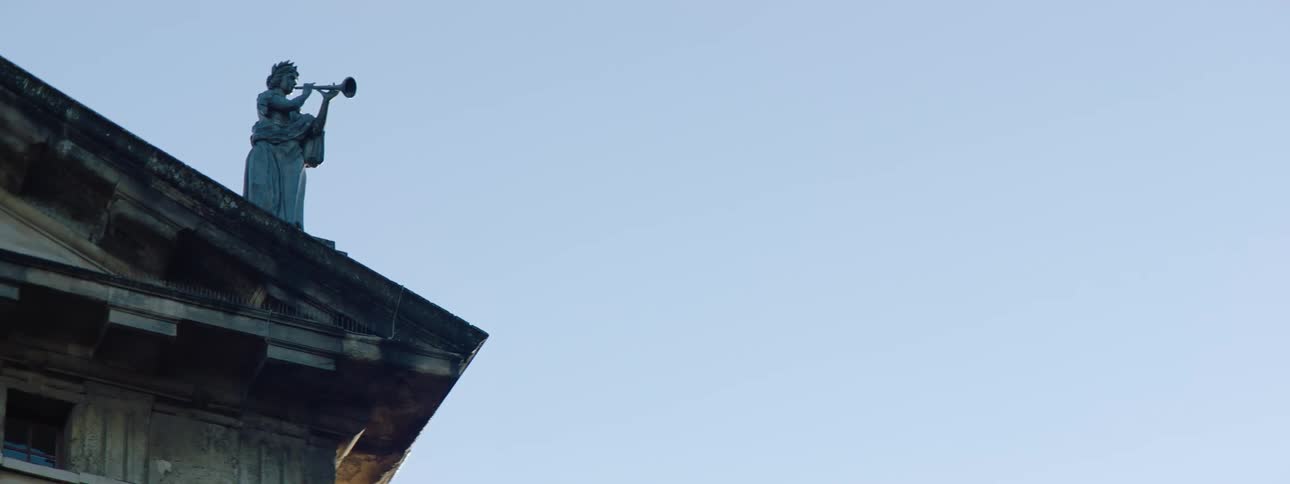 Statue of person playing a horn stands on building roof as water drips slowly