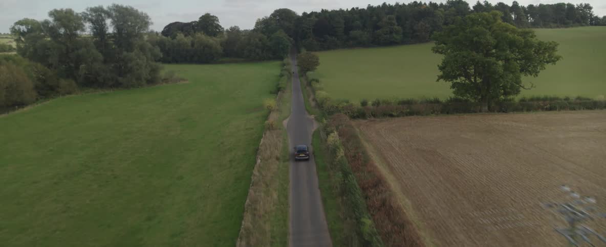 Aerial view of a car driving on a narrow road through the countryside